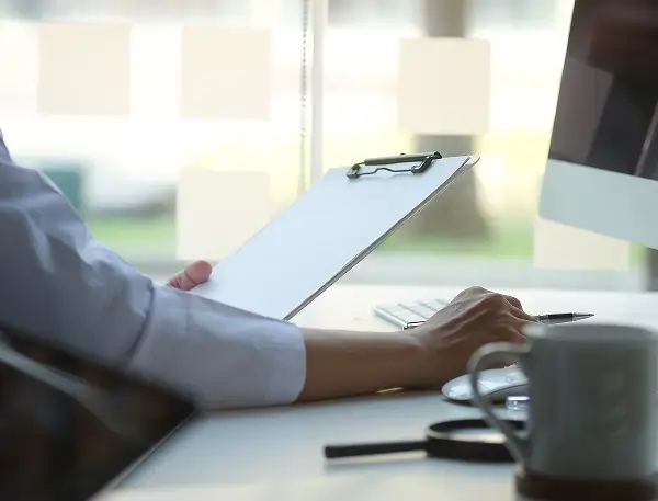 Someone working at a desk, reading a clipboard while typing